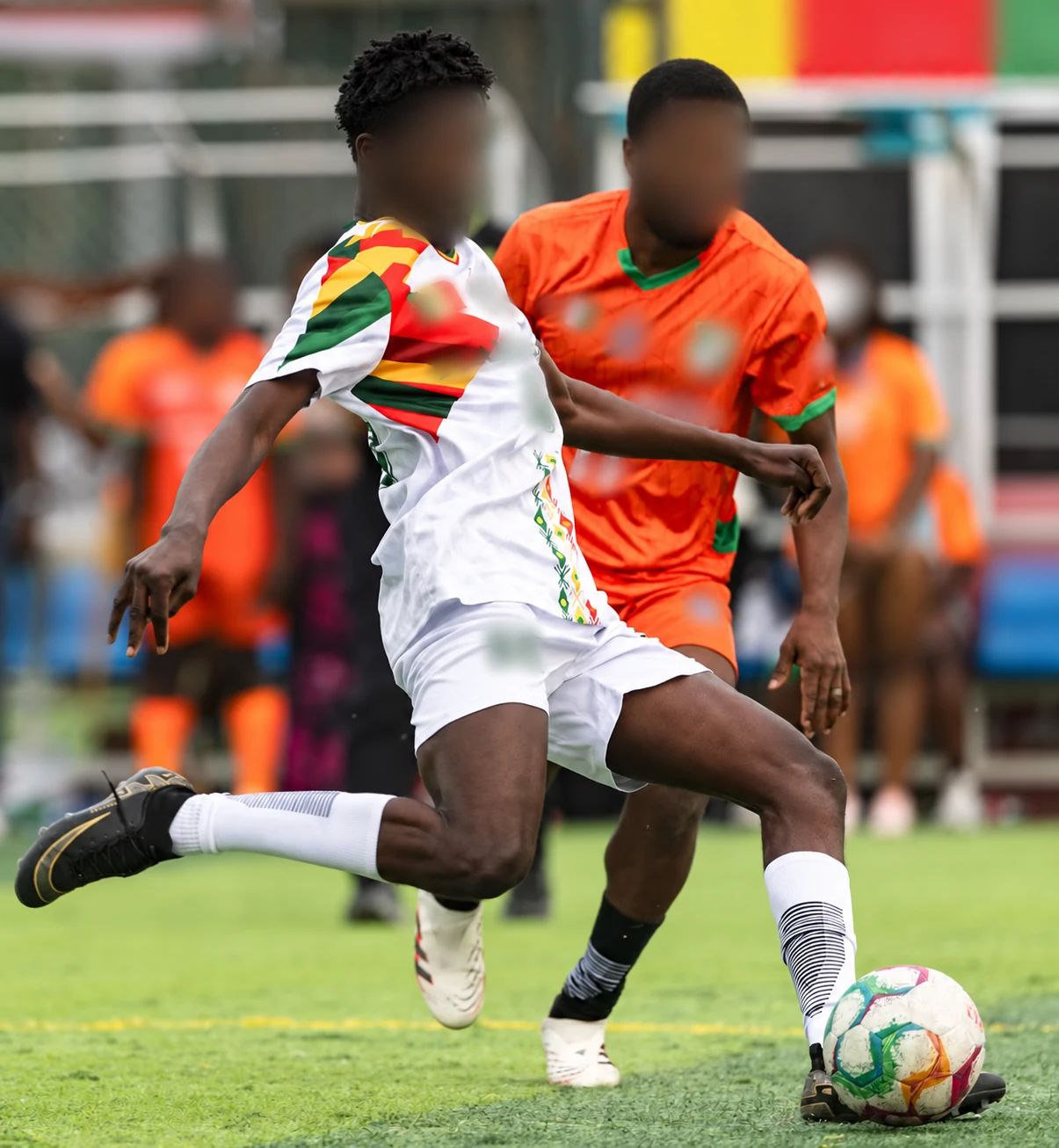 Privacy-edited project image showing white-based multicolour and orange football shirts during play.