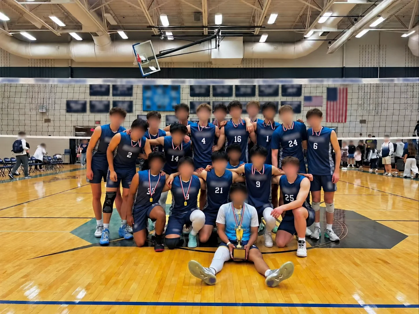 Volleyball team wearing coordinated navy sleeveless uniforms with individual numbers and a contrasting light-blue uniform; faces blurred in the supplied photograph.